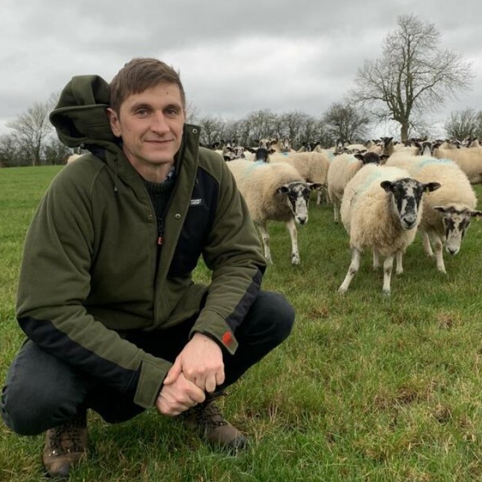 James MacCartney in a field with sheep behind him